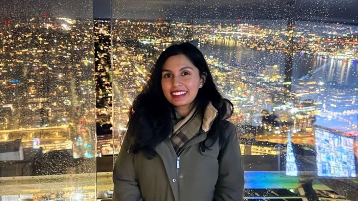 Pace Seidenberg alum Lolita Tiwari posing for a photo in front of a rainy cityscape at night.