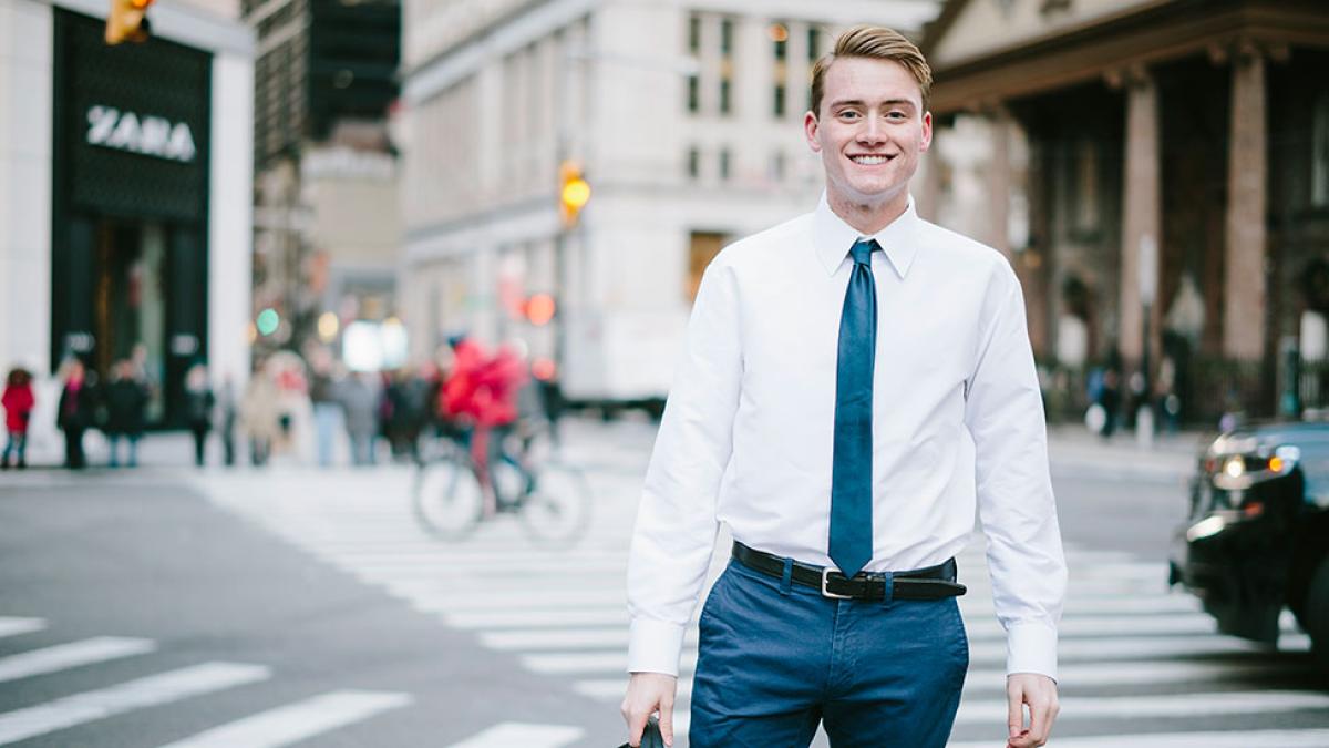 Pace University student dressed in business attire, standing on a street in NYC, smiling at the camera.