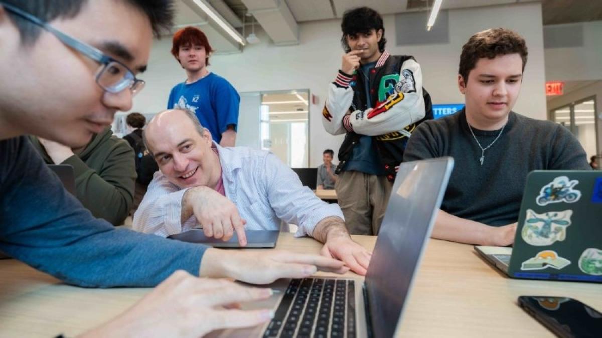 Seidenberg professor Carmine Guida working with a group of students on their laptops.