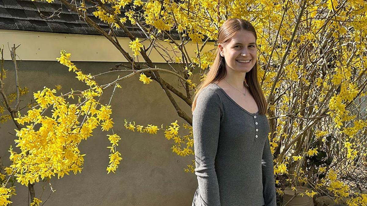 Pace student Natasha Dapaoli stands in front a tree with yellow flowers