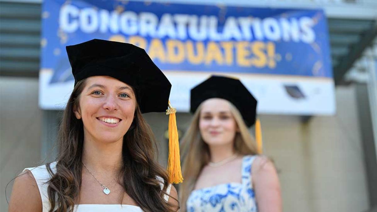 Graduates in graduate caps standing in front of a congratulatory sign