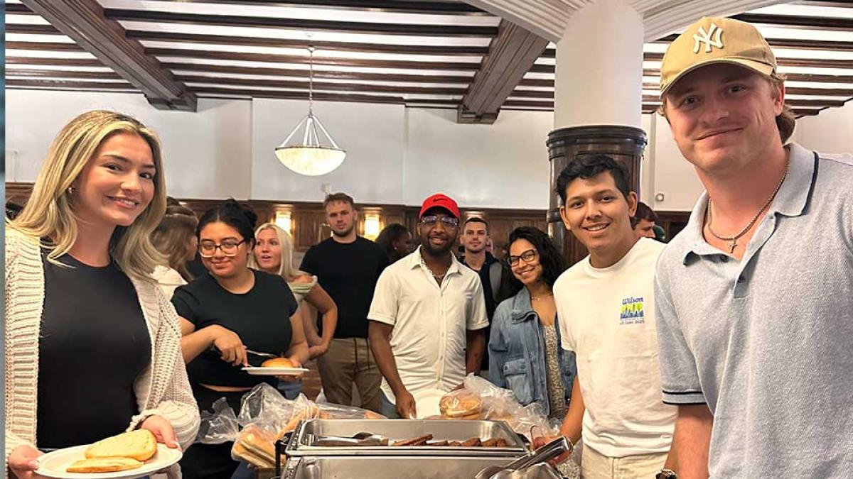 Students in BBQ food line facing camera and smiling