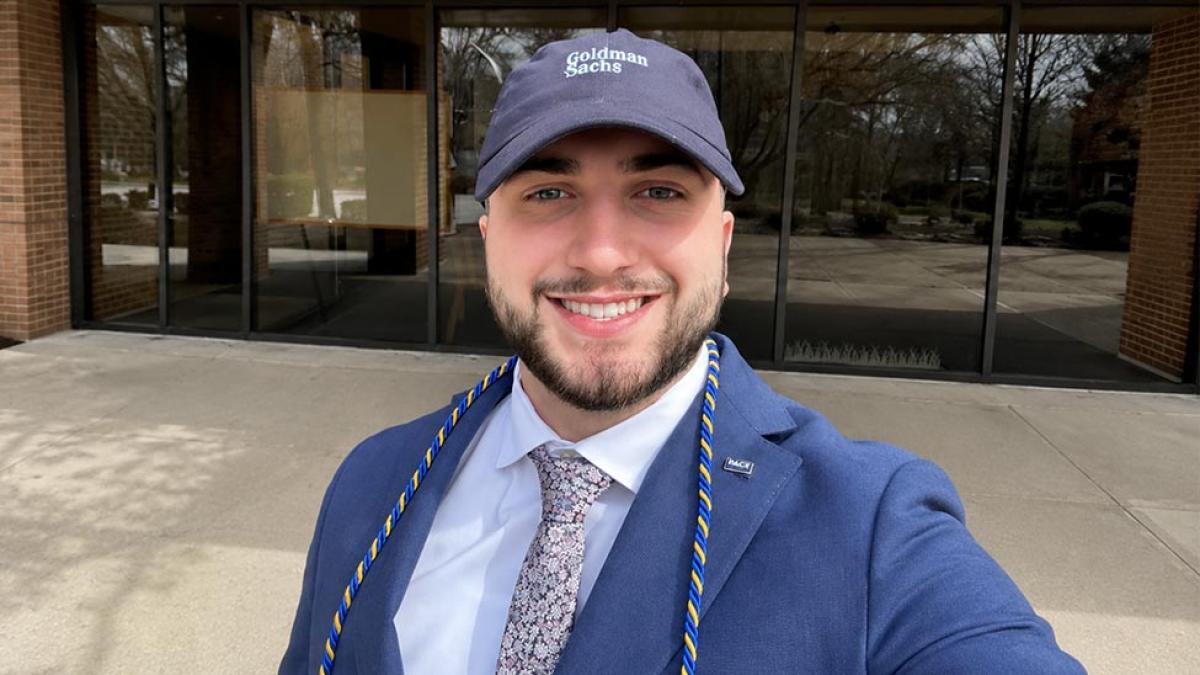 Evan Glusic wearing a suit and a Goldman Sachs baseball cap.