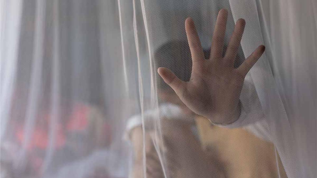 A child’s hand presses against a sheer curtain, partially obscuring their face behind the fabric.