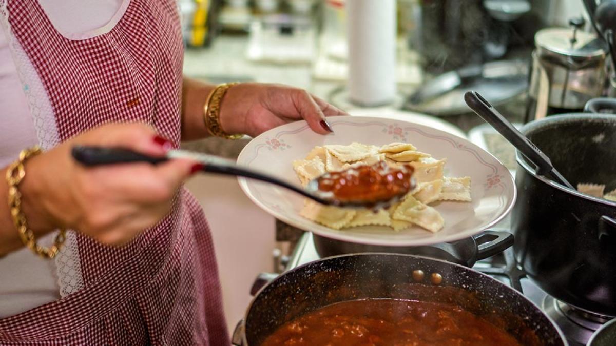 Close-up of a woman in a kitchen dishing up pasta with sauce.