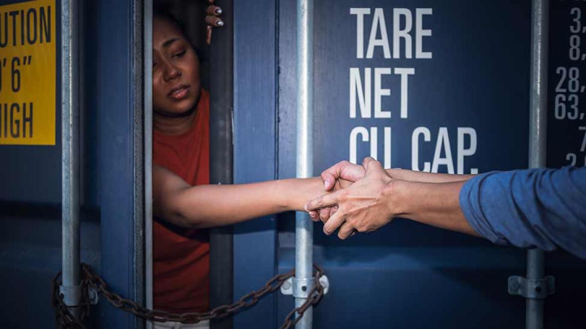 A woman inside a shipping container reaching out to grasping hands.