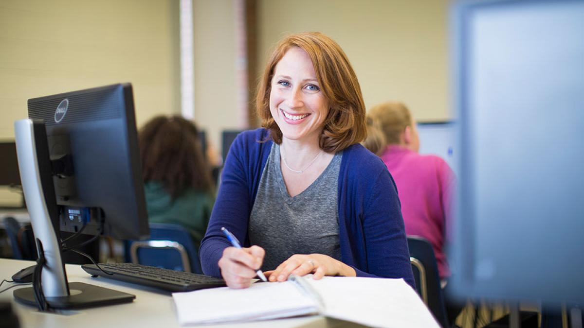 Female Pace University student, smiling at the camera, sitting behind a computer.