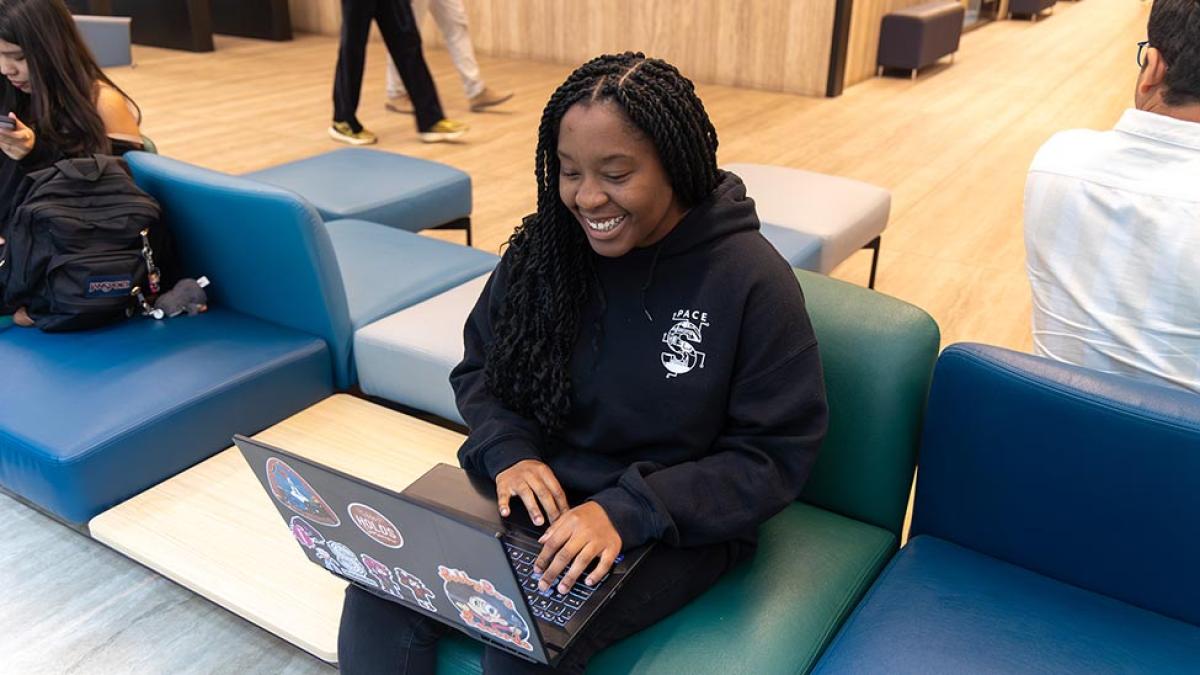 Pace University student sitting in a chair, working on her computer.