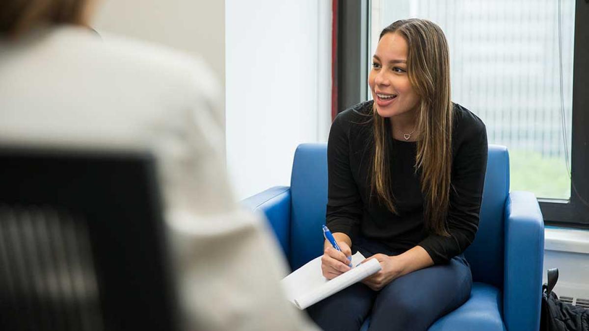 Pace University student sitting in a chair, smiling and talking.