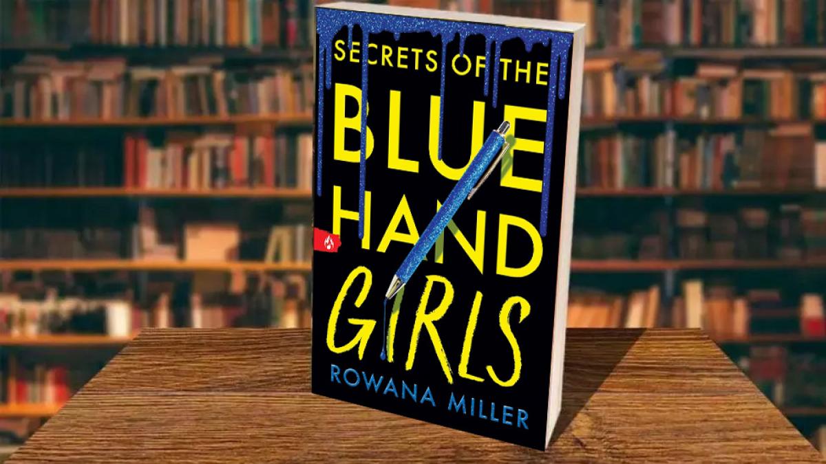 Cover of Rowana Miller's Secrets of the Blue Hand Girls in front of a bookshelf.. The title is written in yellow text and the author's name is written in blue text. Blue ink drips from the top of the image and a blue pen is in the center of the page.