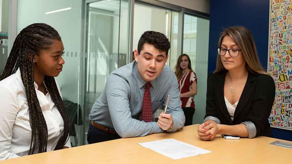 Three Pace University students look over a paper on a table