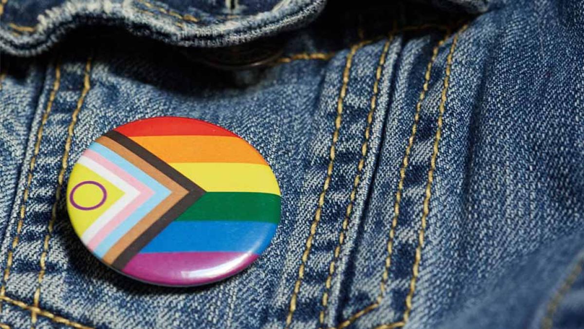 An LGBTQA+ button on a denim jacket.