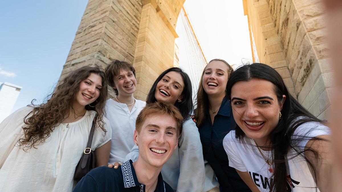 Group of Pace University students taking a selfie in front of the Brooklyn Bridge.