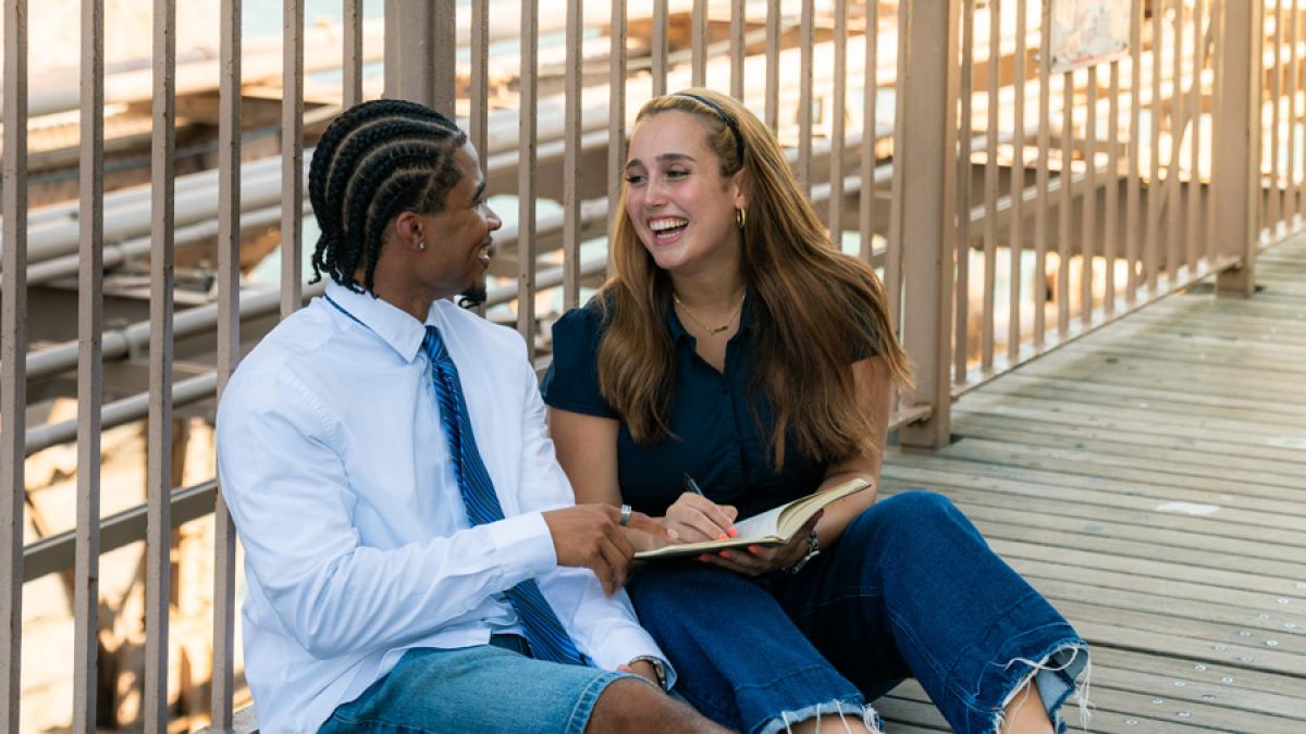 Two Pace University students sitting on the floor in NYC, talking.