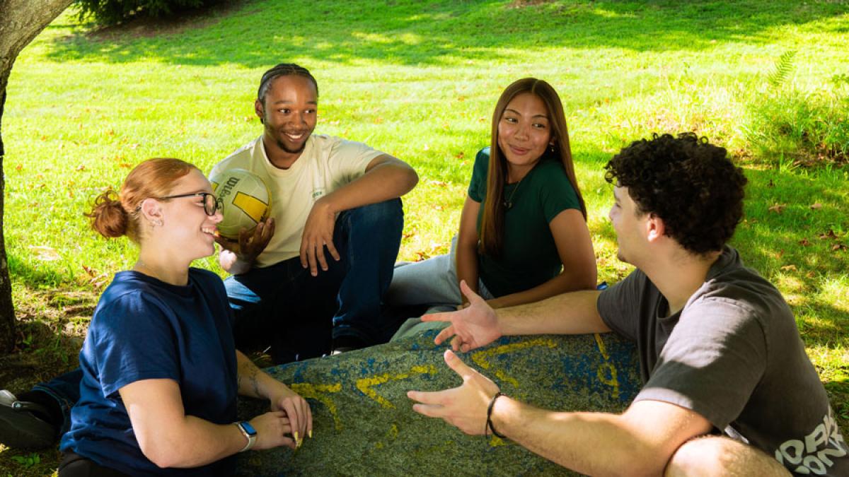 Four Pace University student sitting on the lawn, talking and laughing.