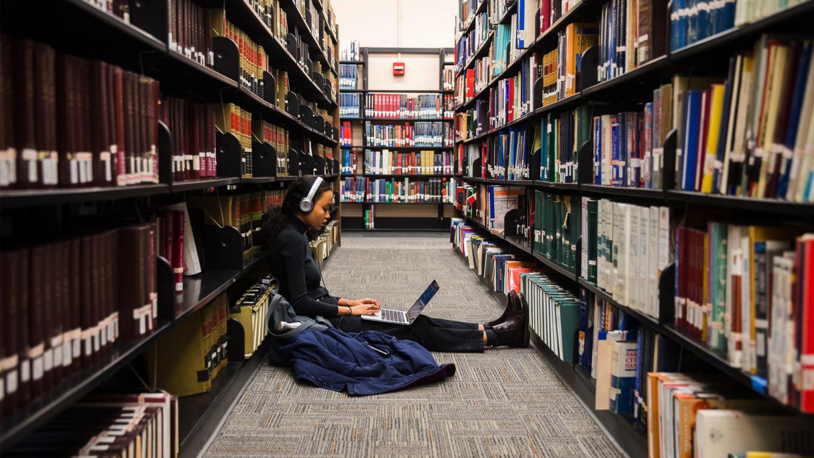 Student sitting on the floor in the library studying.