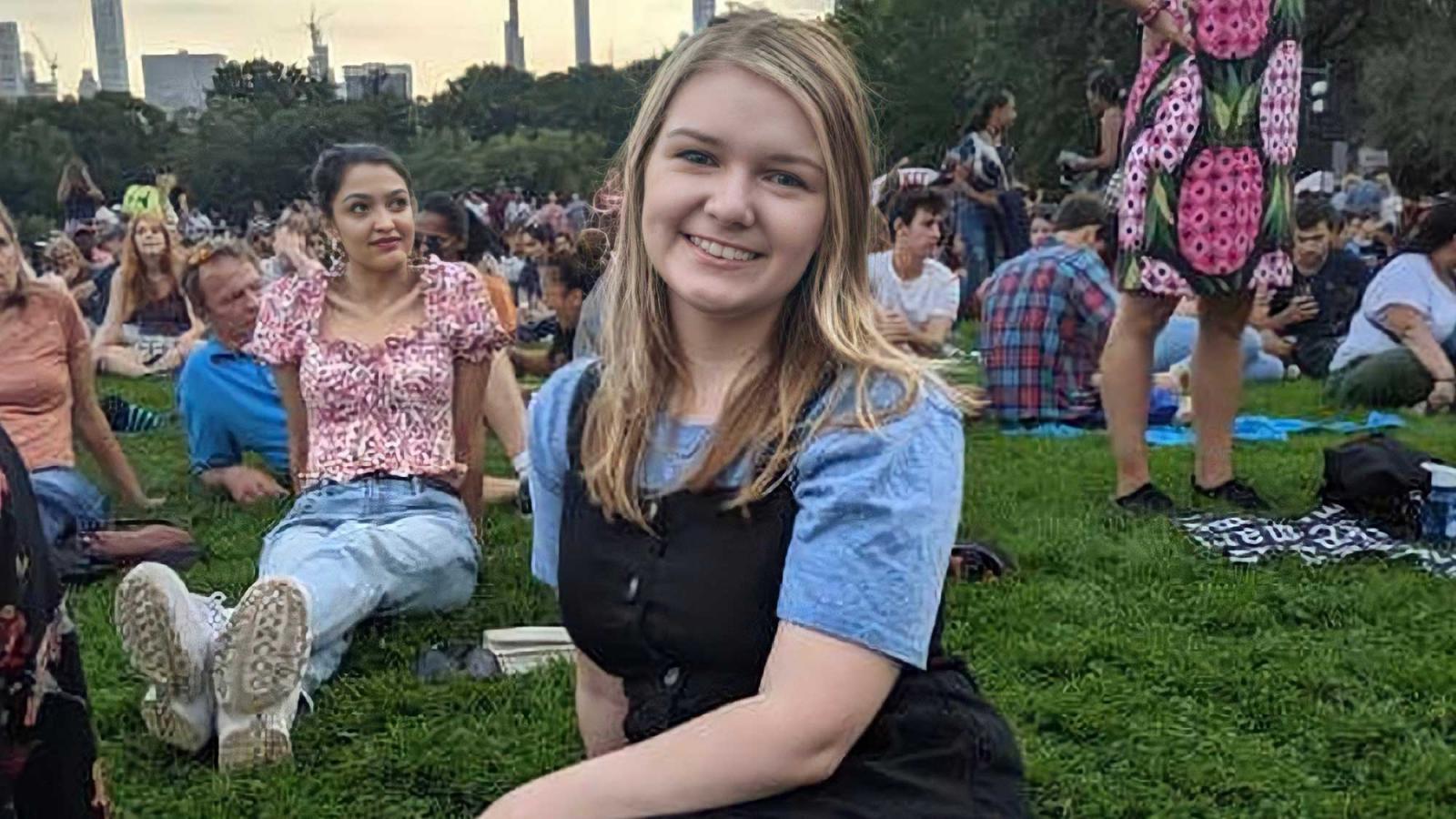 blonde girl sitting on the grass in a crowd