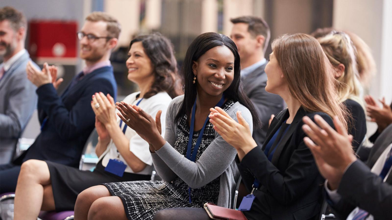 Group of staff members sitting at an event clapping their hands.