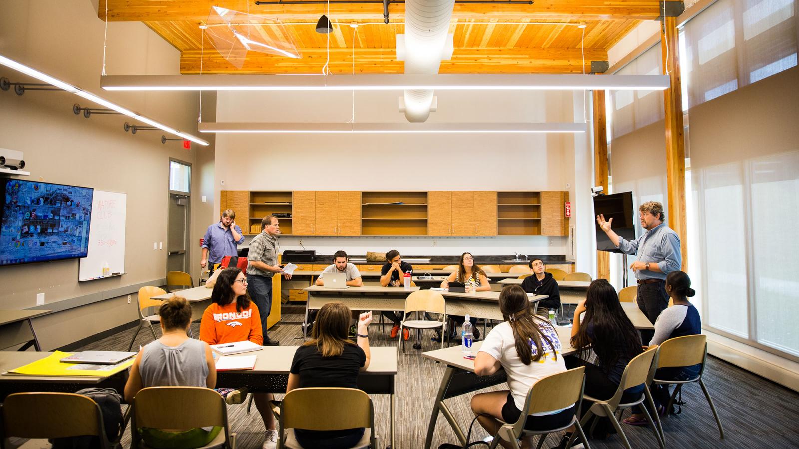 Students sititng in a classroom listening to a teacher.