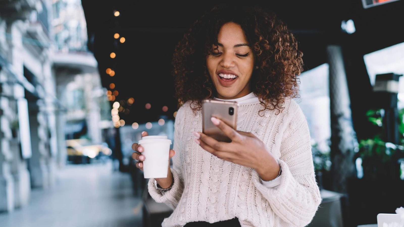 young woman with braces holding a coffee cup and looking at her phone