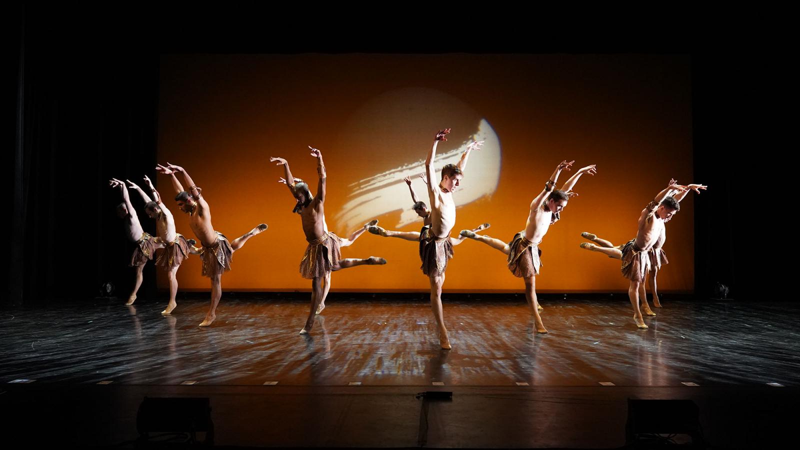 Commercial dance students caught in motion on stage infront of orange background