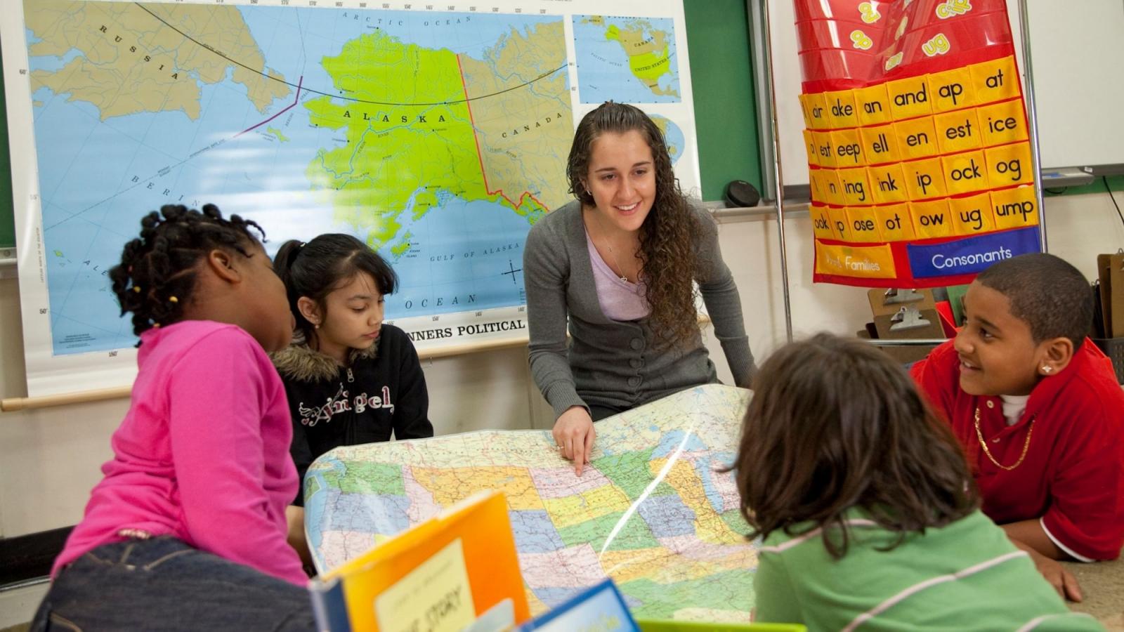 Teacher student classroom looking at a map smiling