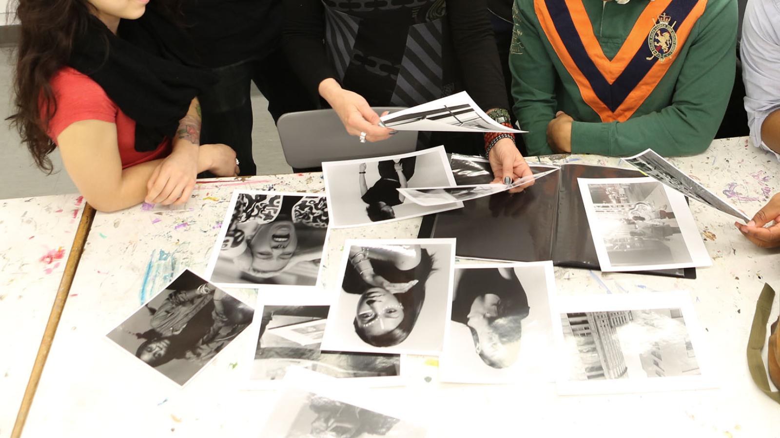 Students and professor looking over printed/developed black and white photos on a white desk