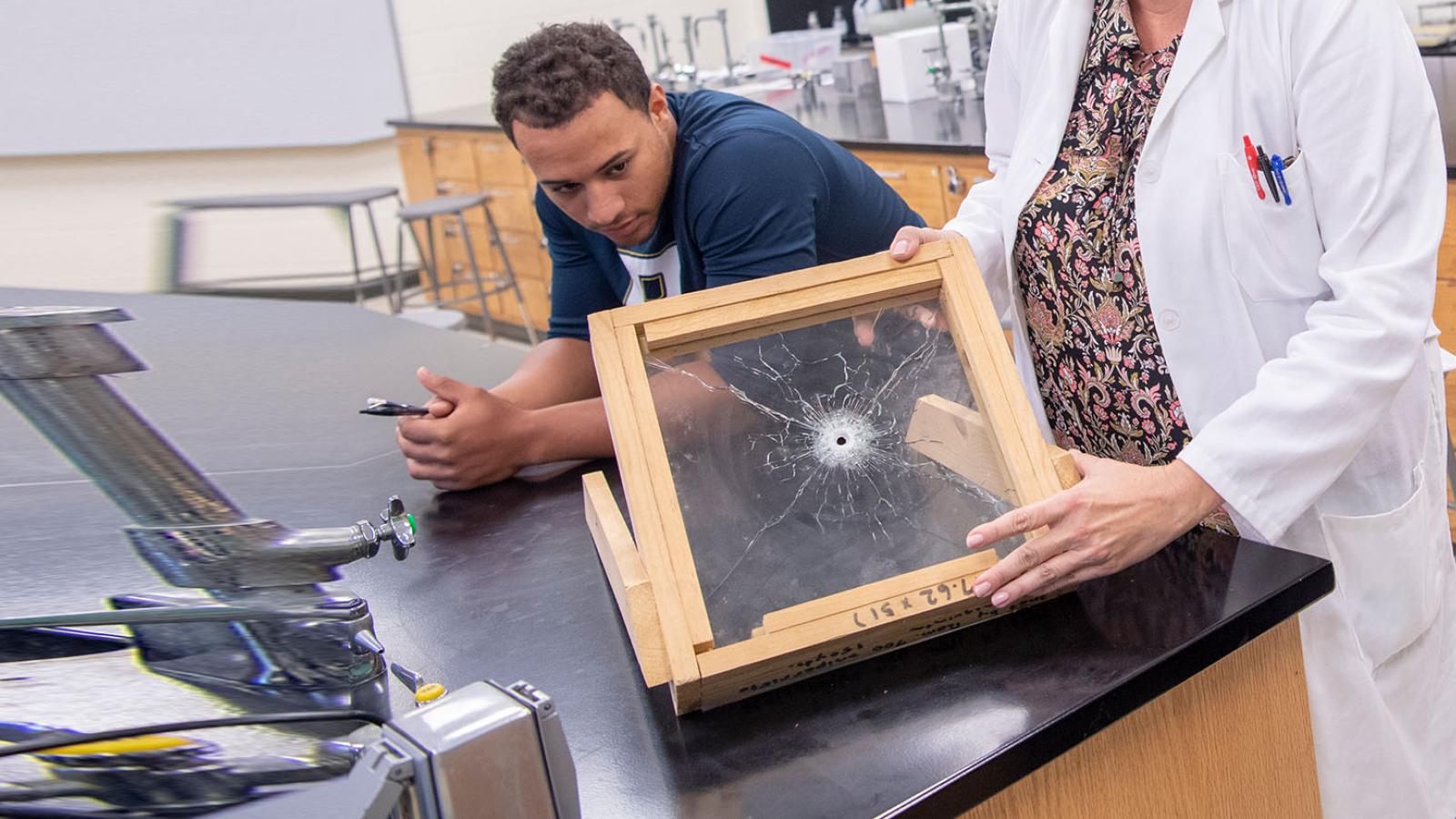 Students examining ballistics glass in a science lab with professor in lab coat