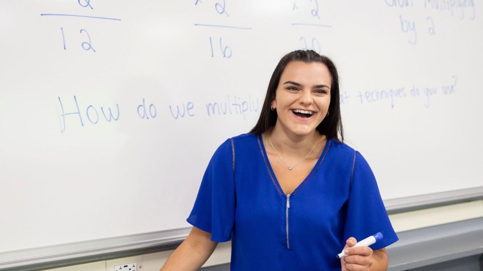college girl laughing in front of whiteboard holding a blue marker