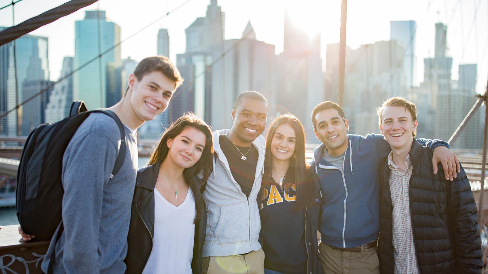 Students standing on the Brooklyn Bridge smiling at the camera.