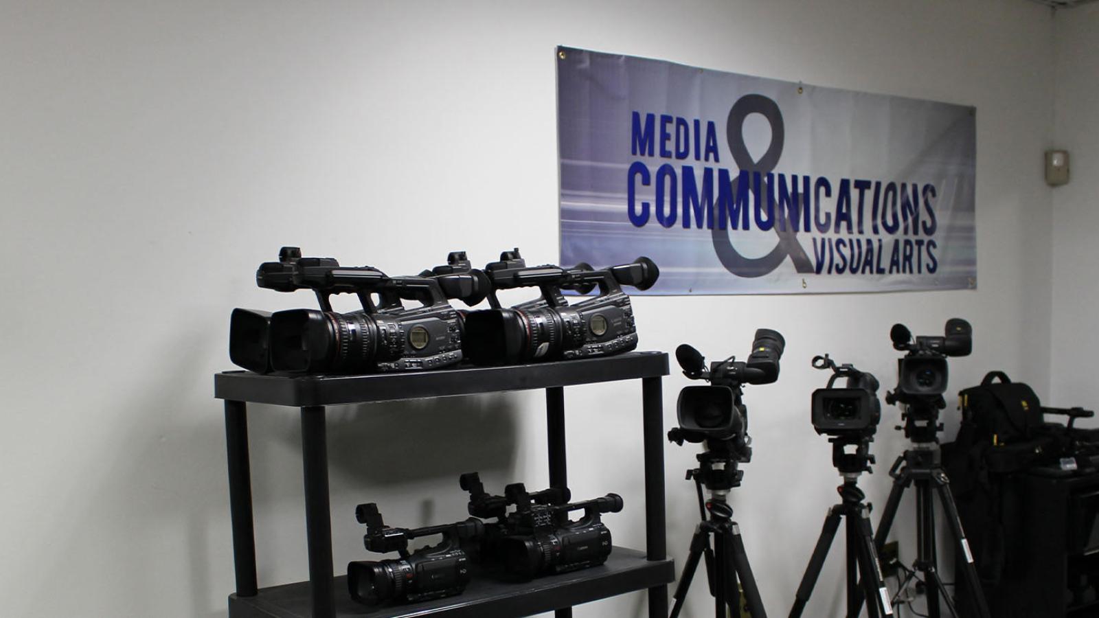Video cameras in a storage room with a Media, Communications, and Visual Arts banner on the wall