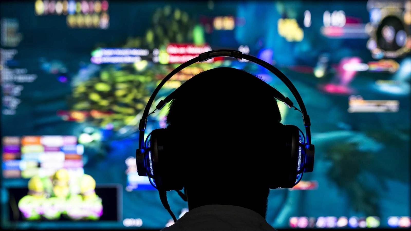 A man with a gaming headset sits in front of a colorful screen