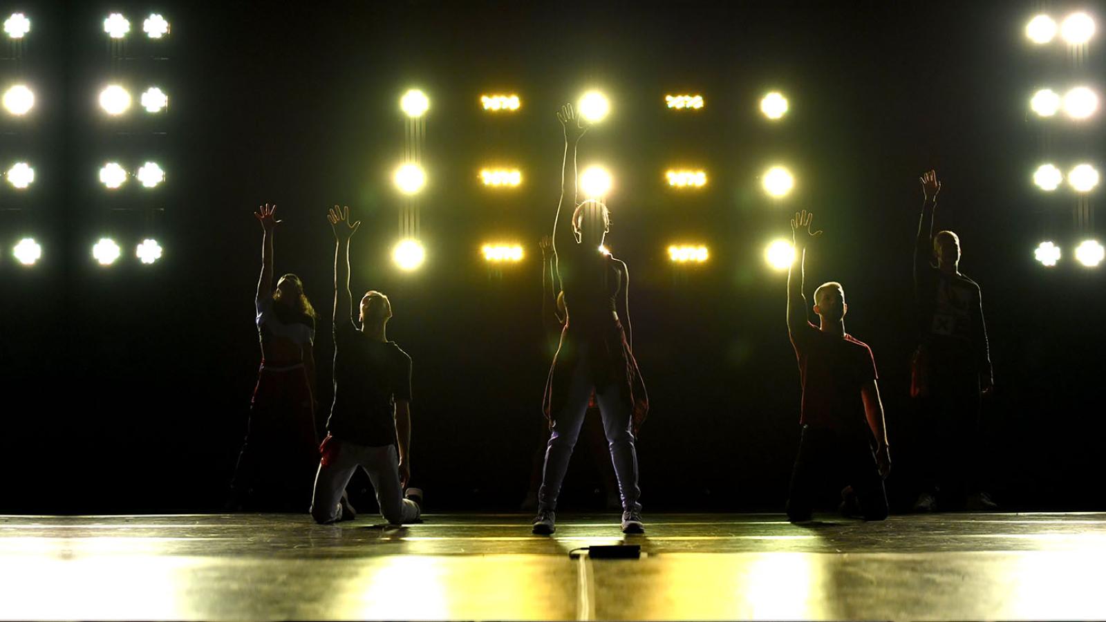 Silhouettes of students on stage infront of yellow lighting