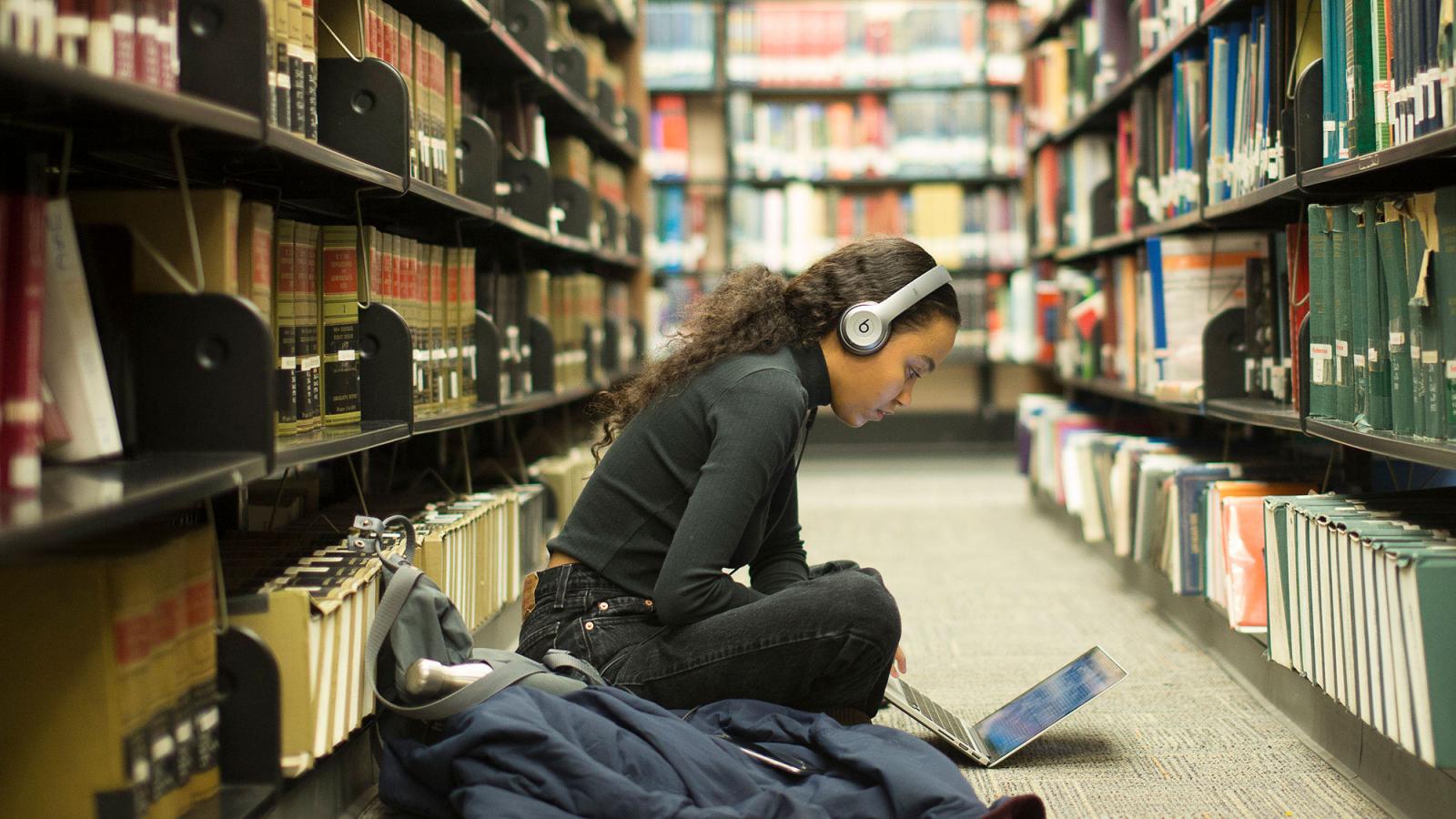 Student sitting on the floor of the library studying.