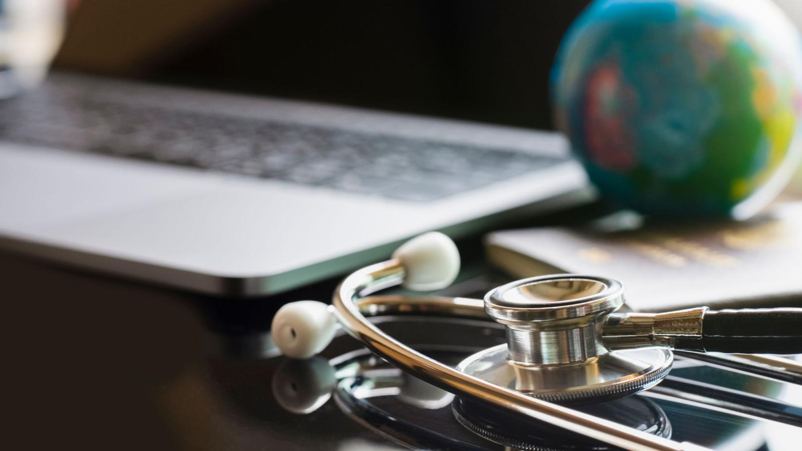 stethoscope and globe on a desk next to a laptop