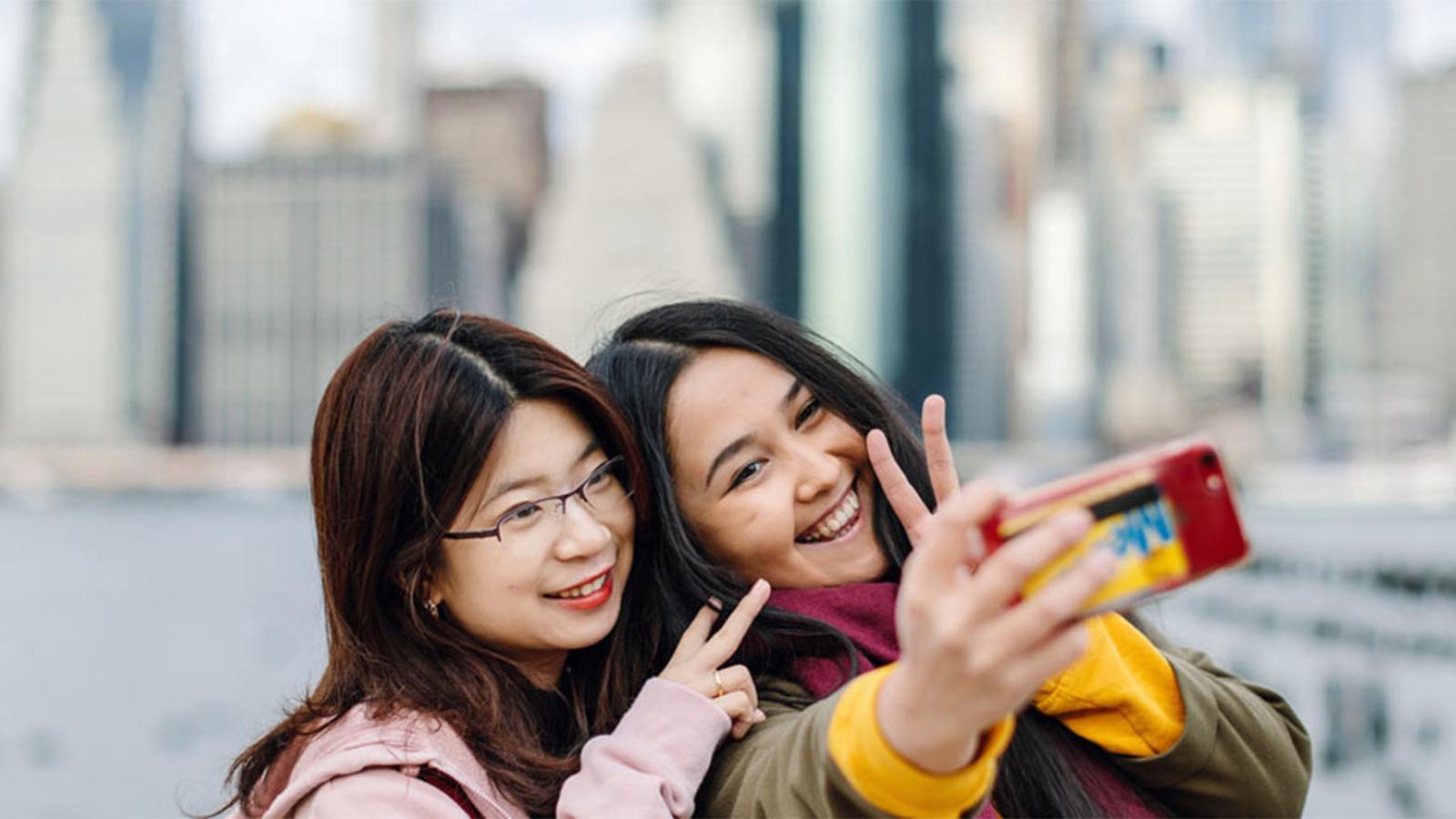 Students take a selfie in front of NYC skyline.