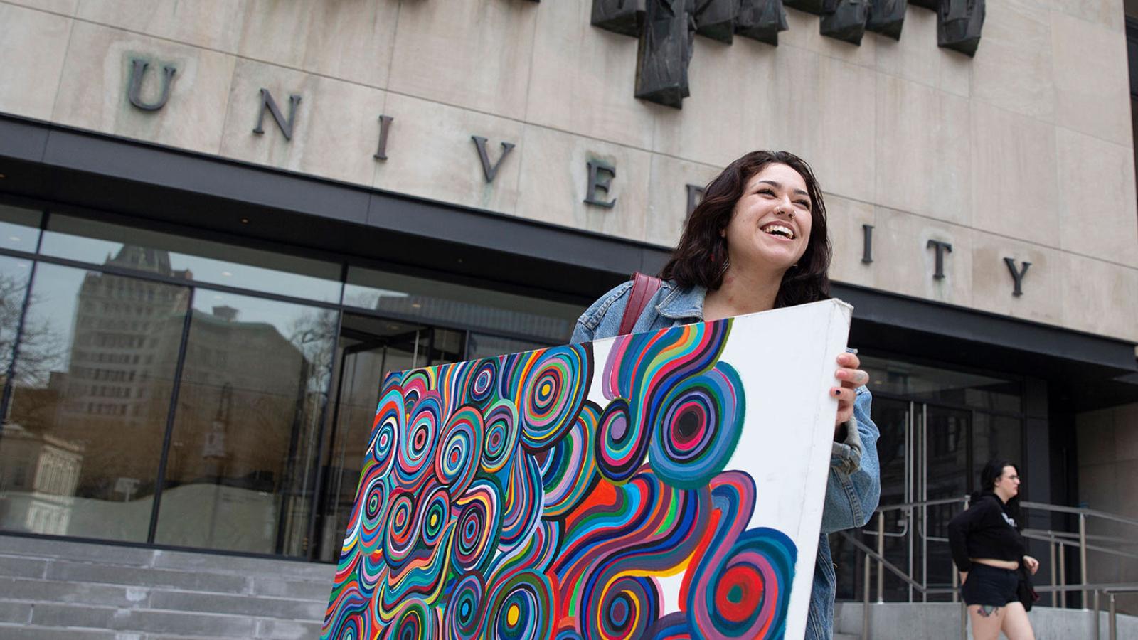 Student carrying a painting in front of 1 Pace Plaza.