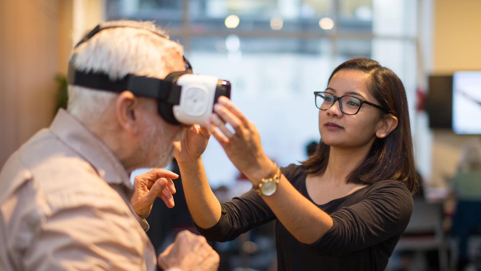 Student helping a man put on a VR headset.