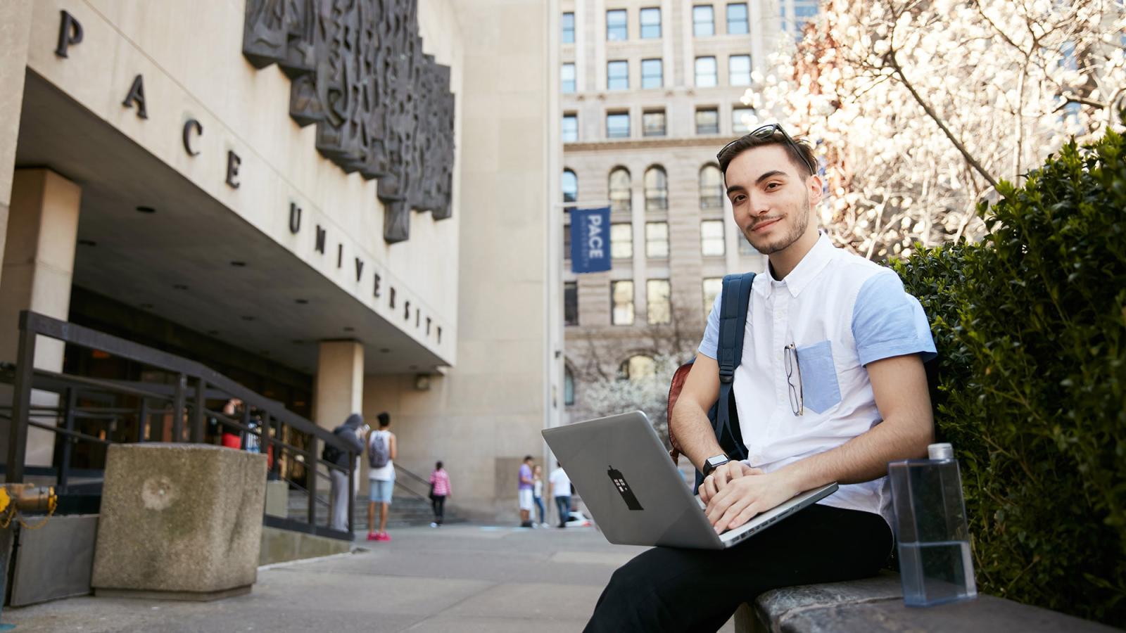 Seidenberg student sitting in front of One Pace Plaza in NYC working on his laptop.