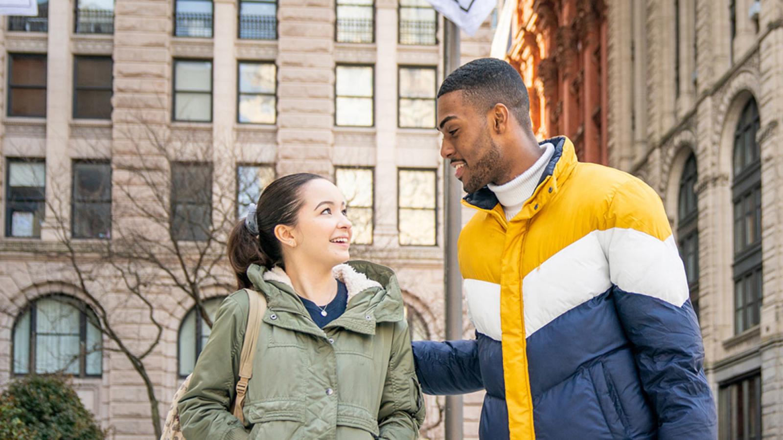 Two Pace University students walking in front of 1 Pace Plaza on the NYC campus.