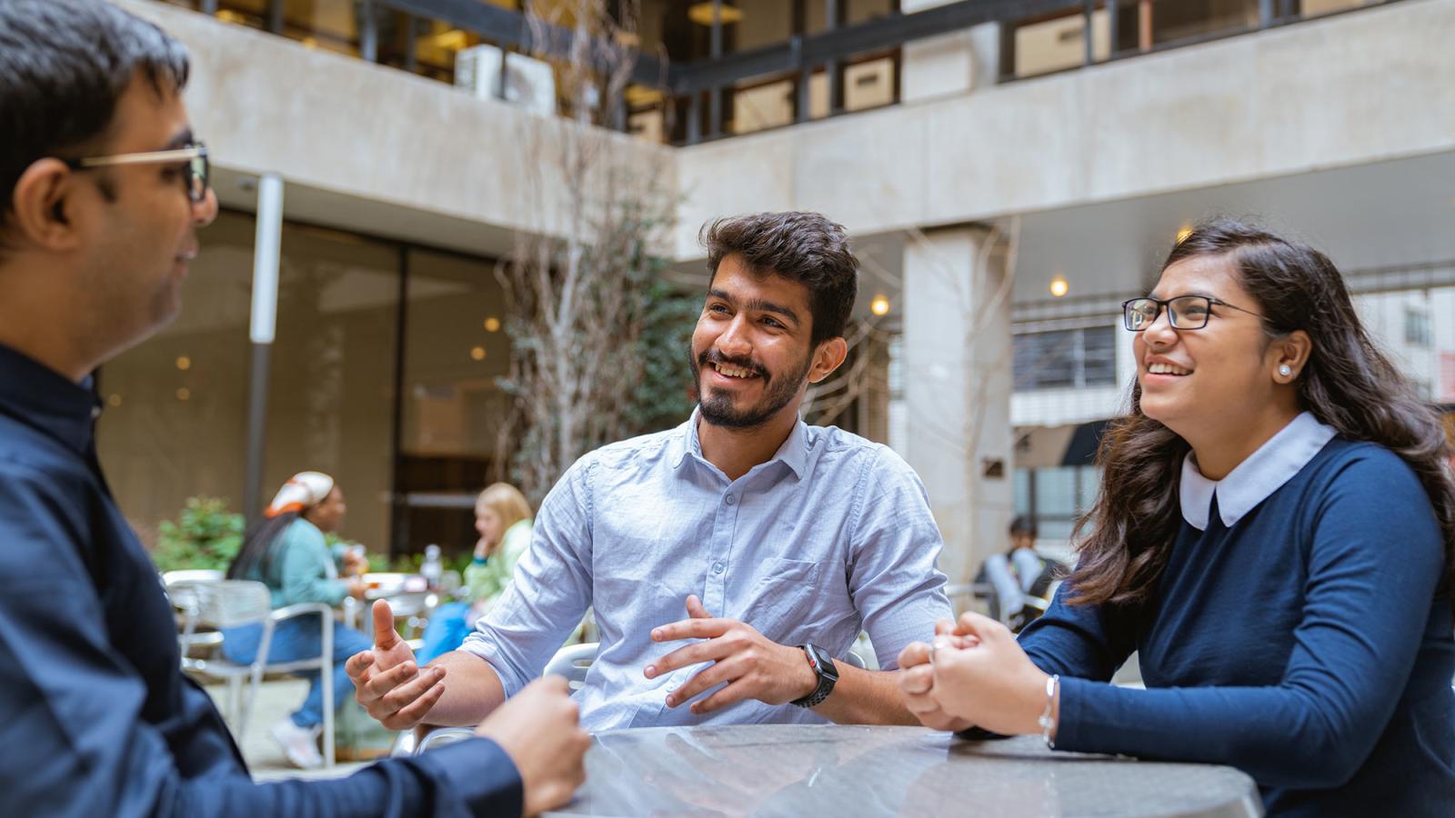 Group of people sitting at a table outside of 1 Pace Plaza talking and laughing.