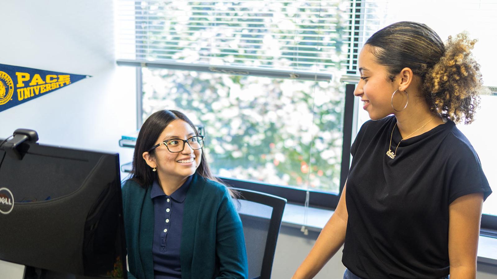 Staff members talking and laughing while sitting behind a computer.