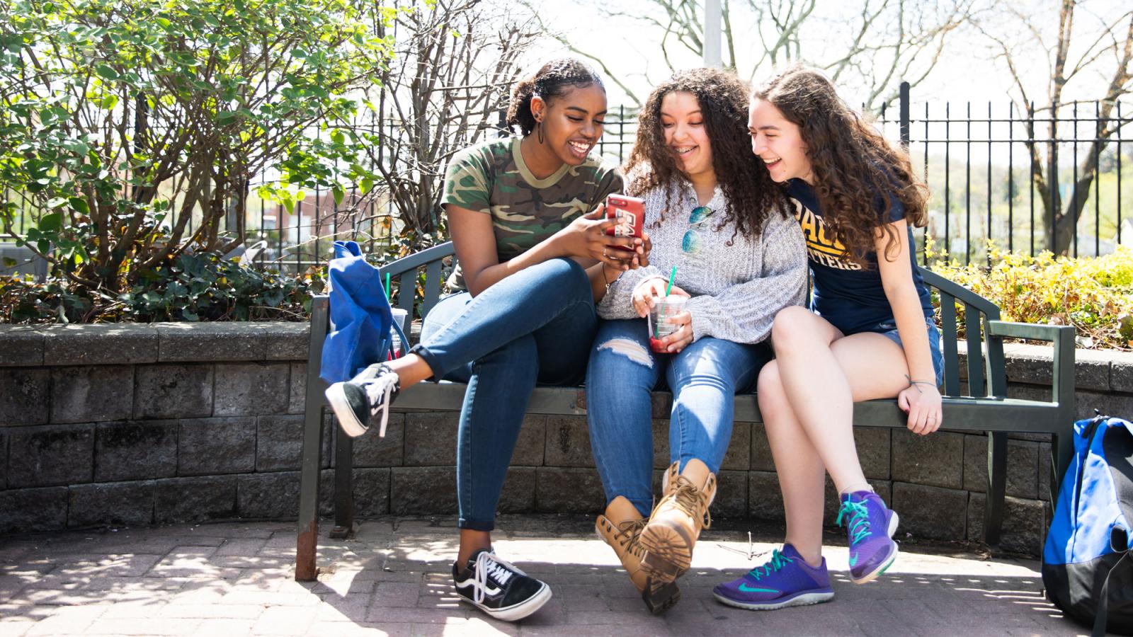 group of women on a bench looking at a mobile phone