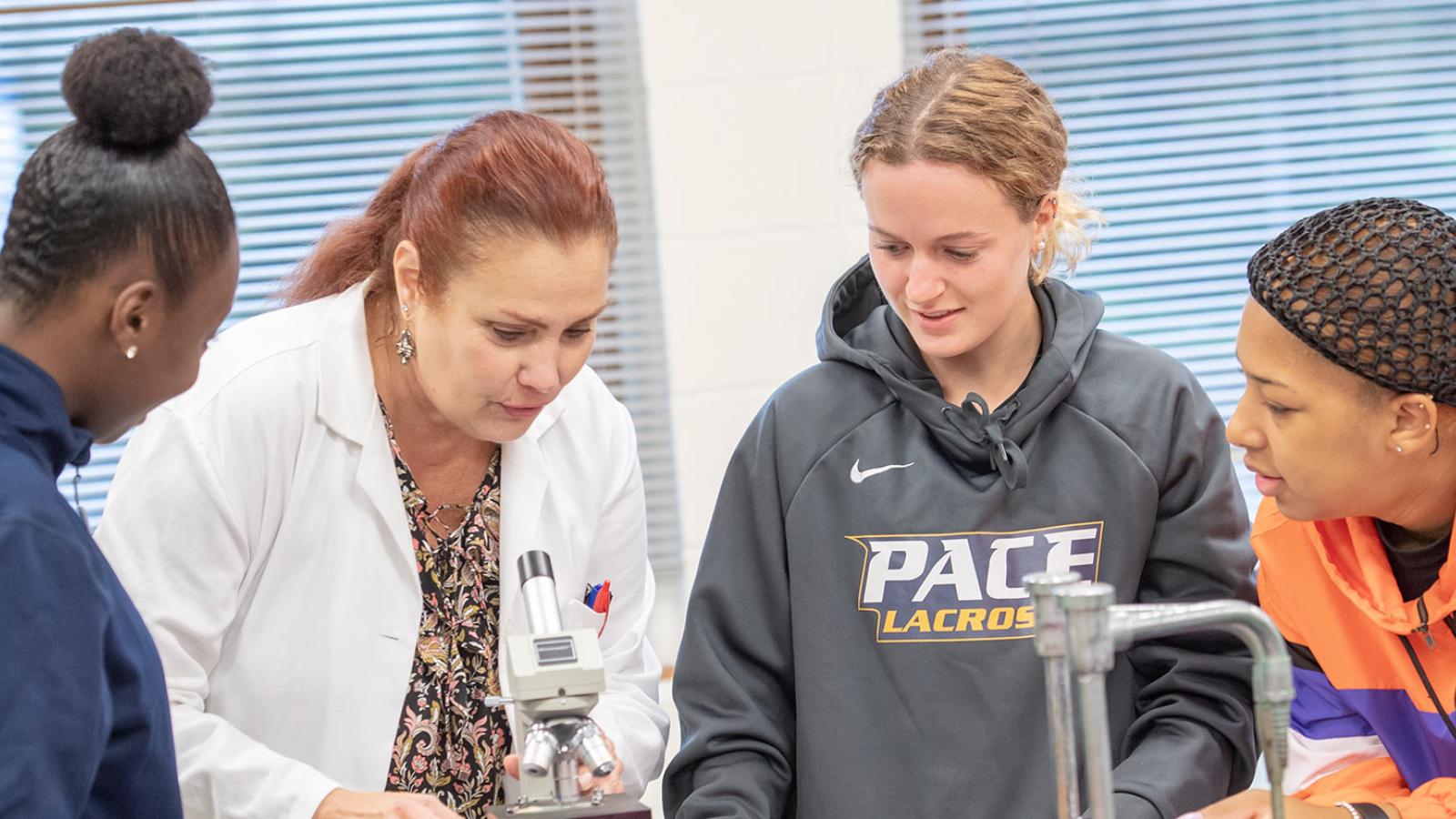 Pace University faculty member showing students a sample on the microscope.