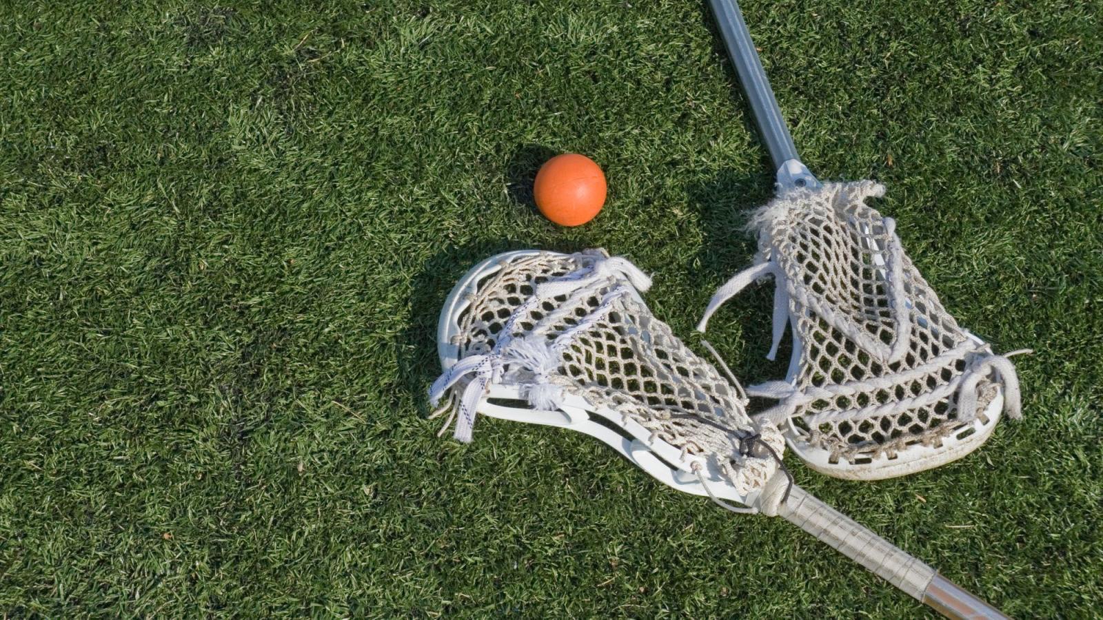 Two lacrosse sticks and a red ball lying on a grassy playing field