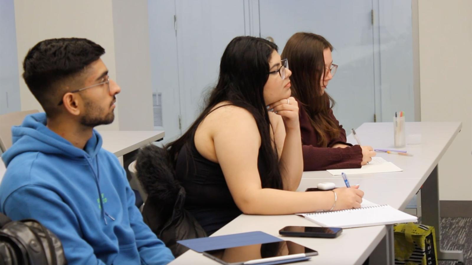 three Pace University students sitting at a table with notebooks and tablet at a Pace Entrepreneurship Studio workshop