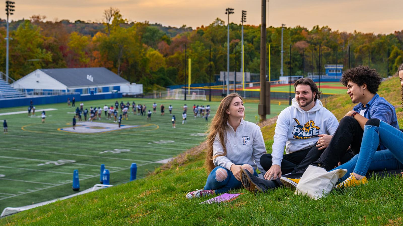 Group os students, sitting on the lawn, watching a football game.