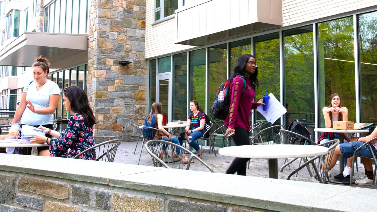 Several pace university students sitting at tables on a patio outside a residential building