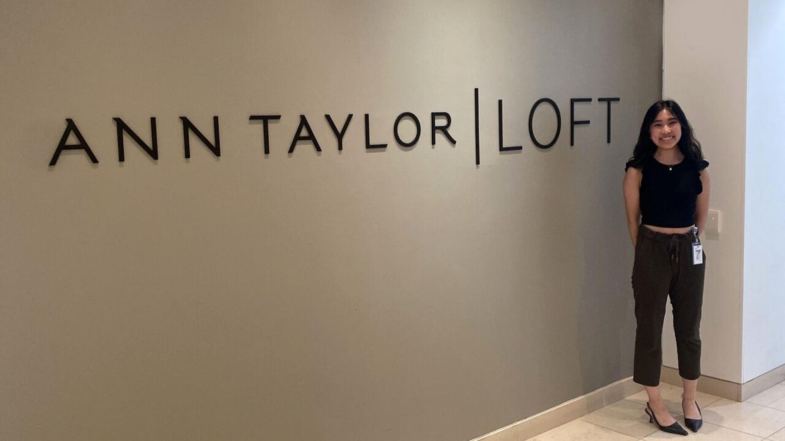 Lubin student Emi Matsumae '25 at her internship office standing in front of the corporate signage for Ann Taylor LOFT