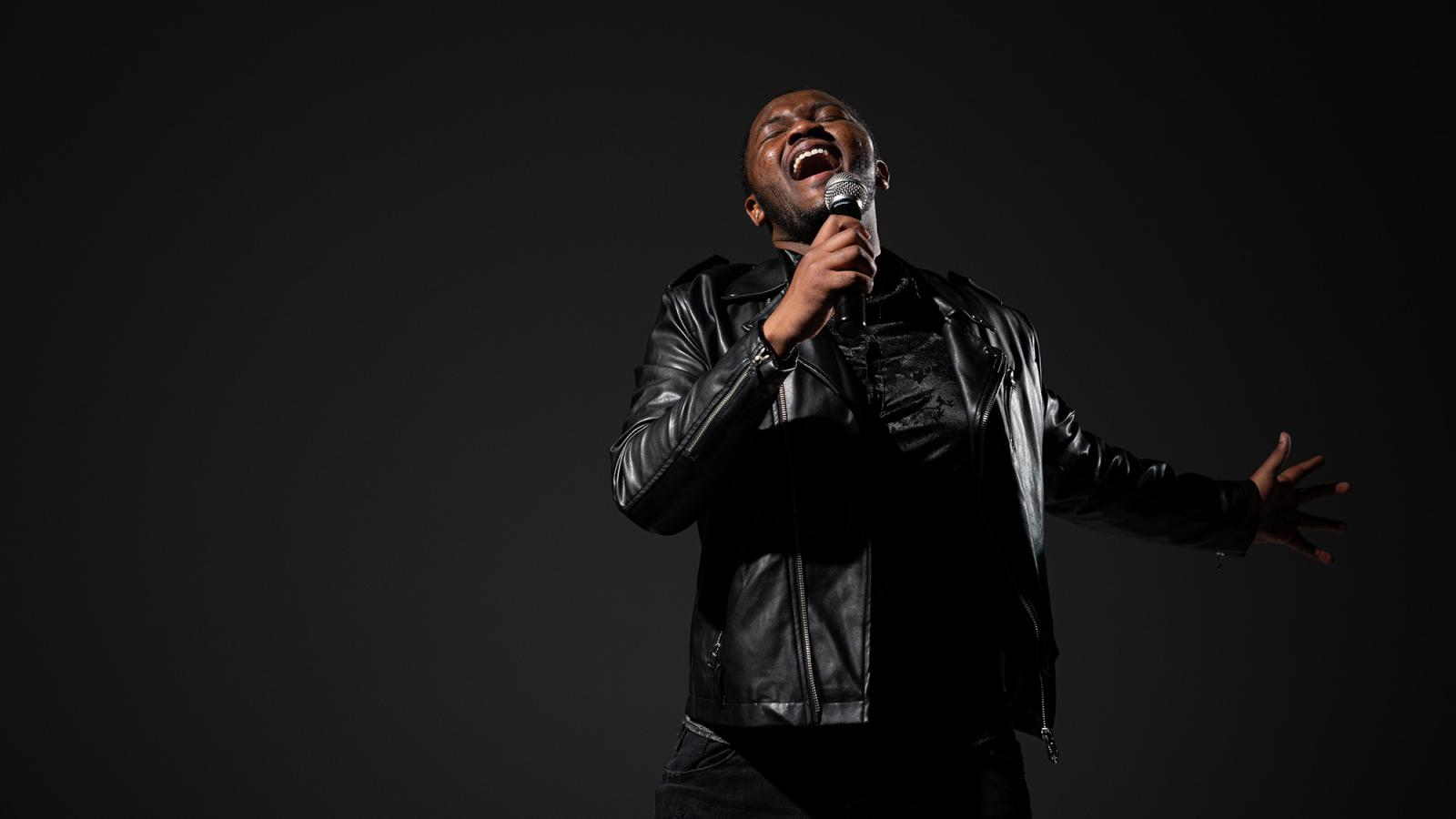 A Pace University student wearing a black jacket sings into a microphone